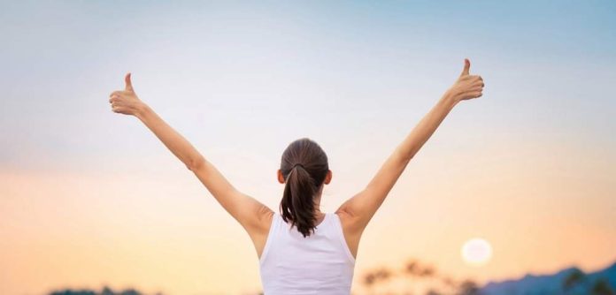 Young woman with arms in the air giving thumbs up.